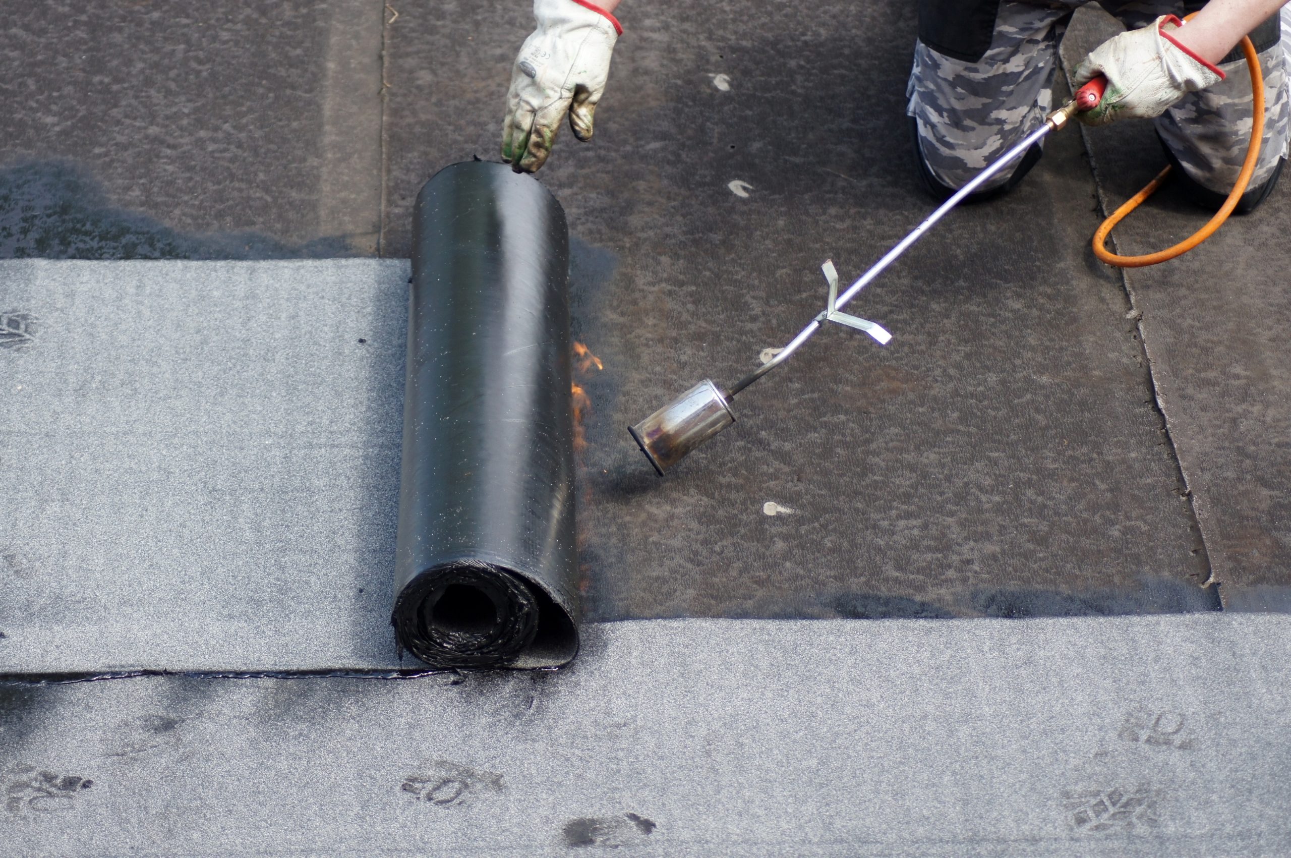 Roofer applying bitumen roofing felt with blow torch